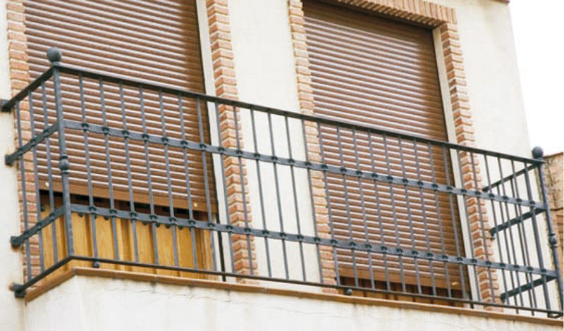 Barandilla de balcón de forja con barrotes verticales en fachada de ladrillo
