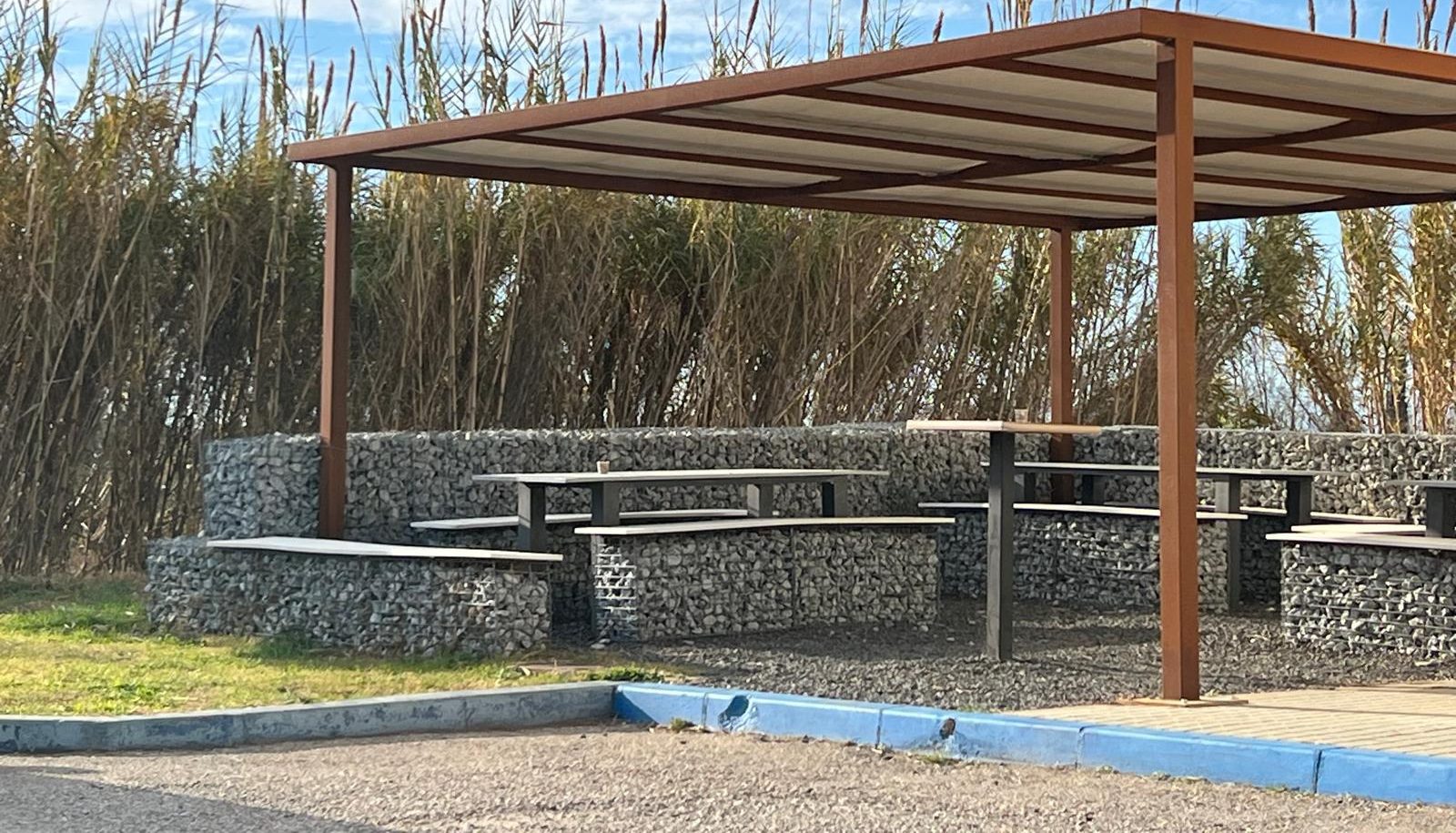 Gaviones de piedra como cerramiento y contención en zona exterior con pérgola y mesas