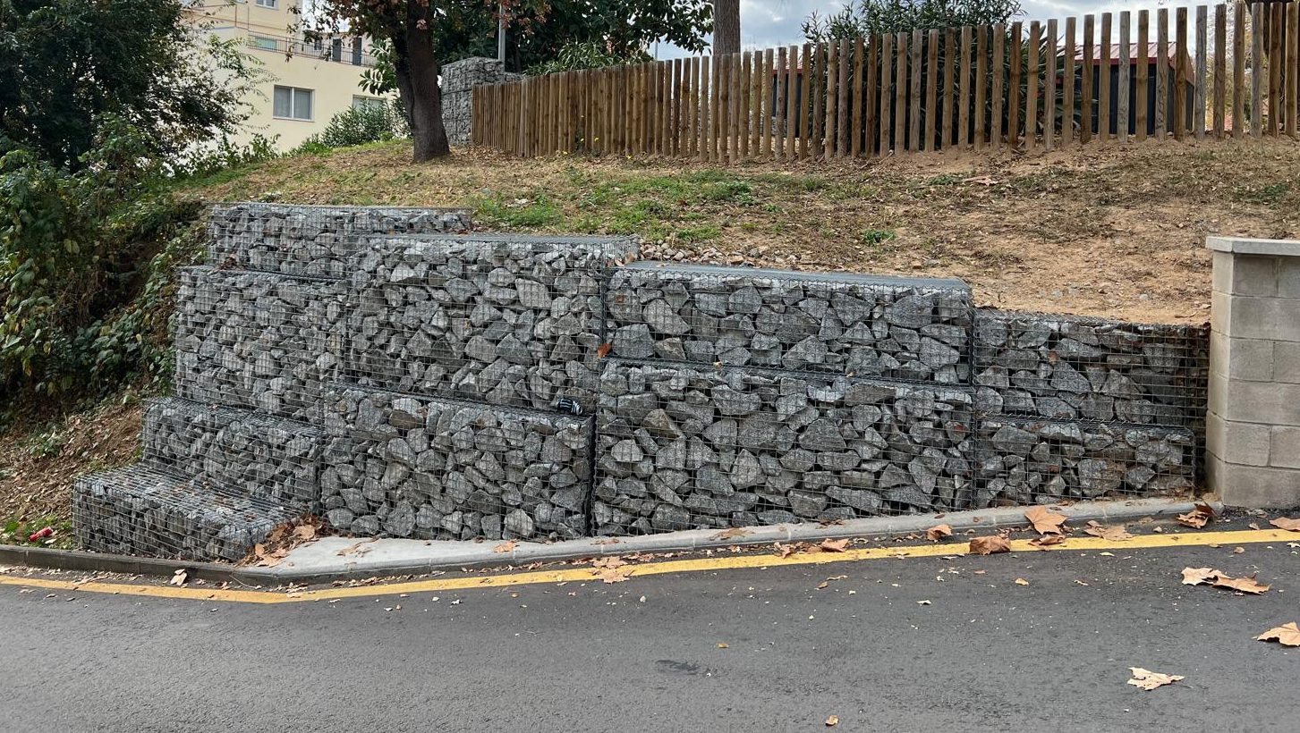 Muro de contención escalonado con gaviones de piedra junto a una calzada