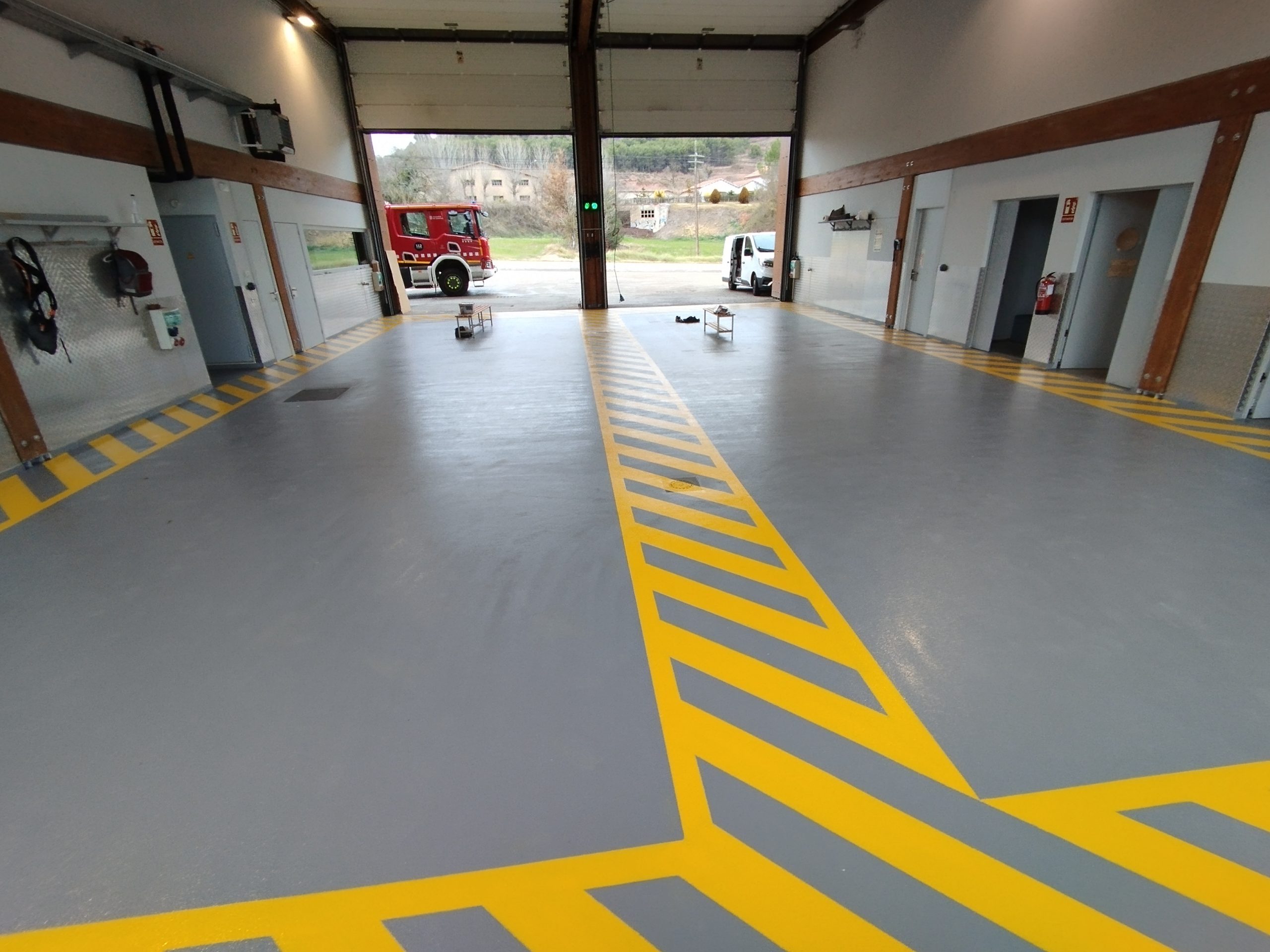 Pavimento continuo gris con señalización amarilla para garaje técnico, parque de vehículos, taller o zona de mantenimiento