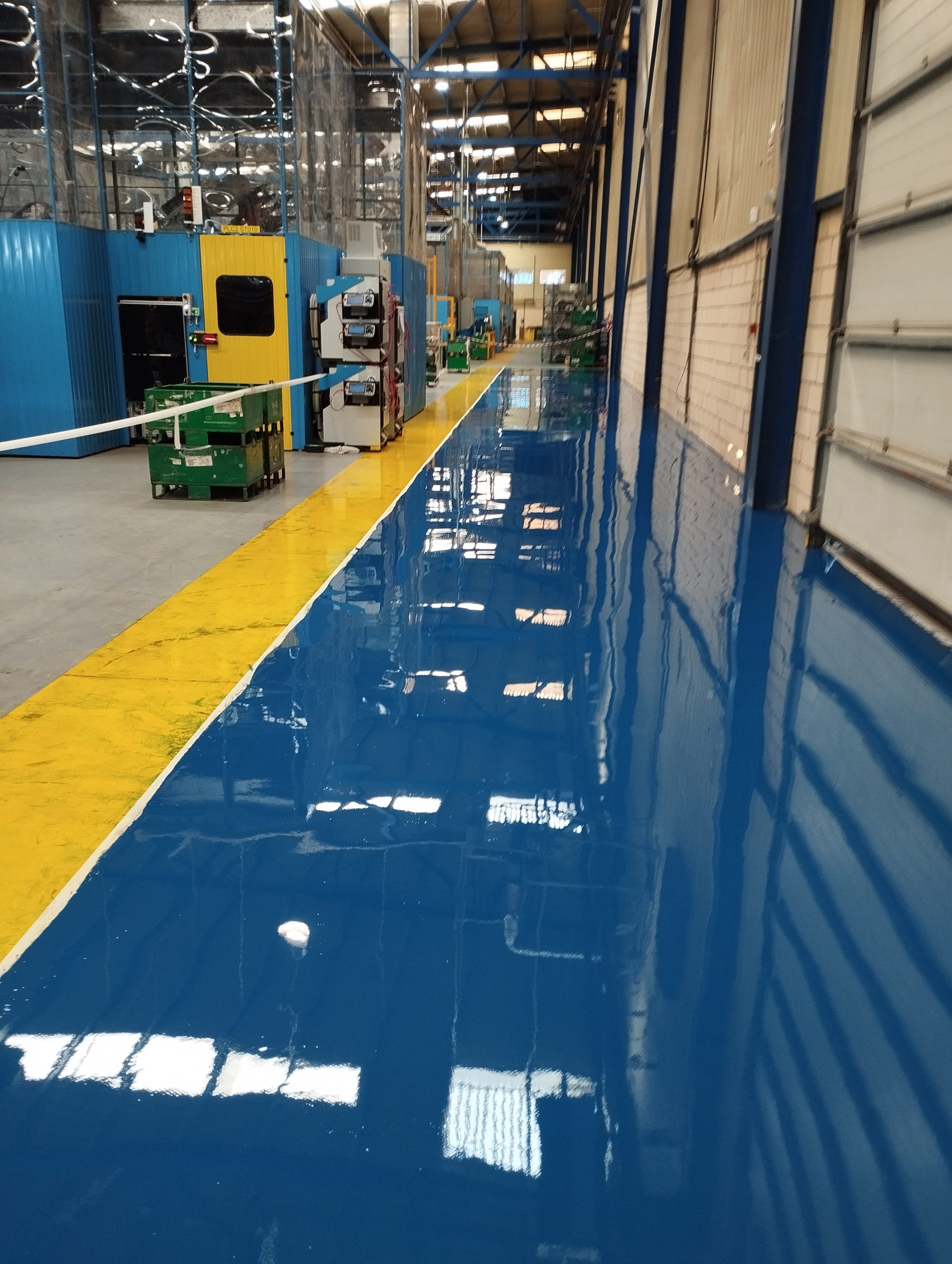 Pavimento epoxi azul brillante con franja amarilla de seguridad para separar zonas de trabajo, circulación y paso de personal
